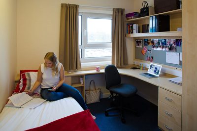 a woman sitting on a bed in a student bedroom